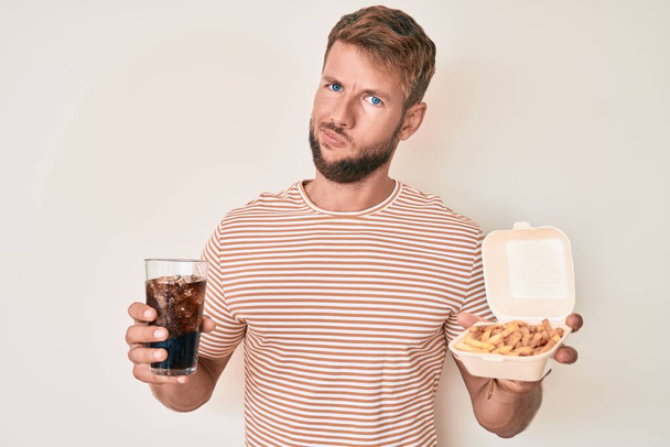 Giovane uomo caucasico mangiare fast food in faccia shock, cercando scettico e sarcastico, sorpreso a bocca aperta  - Foto, immagini