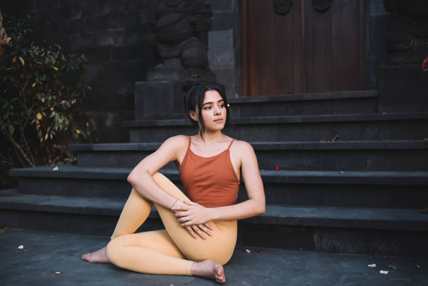 Calm tranquil caucasian female in active wear sitting in yoga pose near door on retreat satisfied with relax and recreation, young girl sitting in asana enjoying harmony keeping healthy lifestyle - Photo, Image
