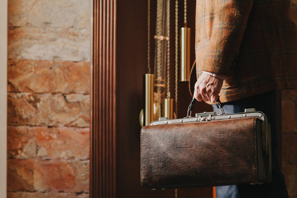 master watchmaker stands in front of an antique grandfather clock. Holds a valise with tools in his han - Photo, Image