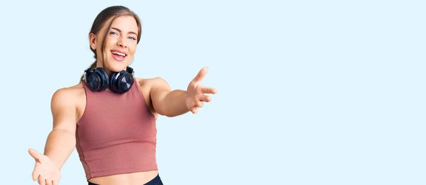 Красива біла молода жінка в спортивному одязі і використовує навушники усміхнені веселі пропонують руки, що допомагають і приймають
.  - Фото, зображення