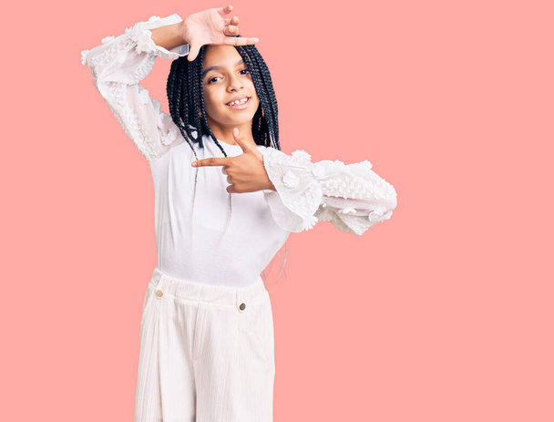 Aranyos afro-amerikai lány alkalmi fehér pólót visel mosolygós így keret kezek és ujjak boldog arcát. kreativitás és fényképezés koncepció.  - Fotó, kép