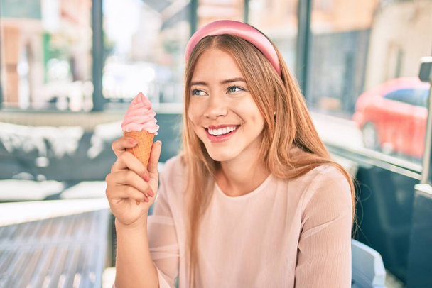 Mladý kavkazský dívka usměvavý šťastný jíst zmrzlinu sedí na kavárně terasa. - Fotografie, Obrázek