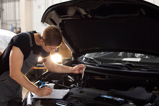 handsome caucasian guy is making notes while repairing hood of car - Foto, imagen