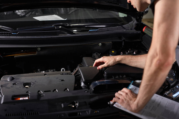 handsome caucasian guy is making notes while repairing hood of car - Foto, Imagen