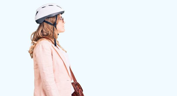 Young caucasian woman wearing bike helmet and leather bag looking to side, relax profile pose with natural face with confident smile.  - 写真・画像