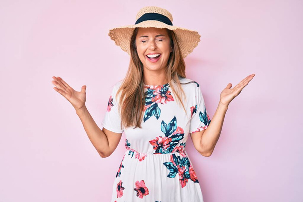 Középkorú spanyol nő nyári kalapban ünnepli őrült és őrült siker felemelt karokkal és csukott szemmel sikoltozó izgatott. győztes koncepció  - Fotó, kép