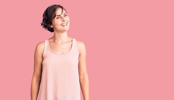 Beautiful young woman with short hair wearing casual style with sleeveless shirt looking away to side with smile on face, natural expression. laughing confident.  - Photo, Image