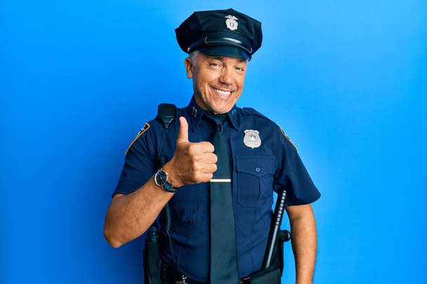Guapo hombre maduro de mediana edad con uniforme de policía haciendo un gesto feliz pulgares hacia arriba con la mano. aprobando la expresión mirando a la cámara mostrando éxito.  - Foto, Imagen