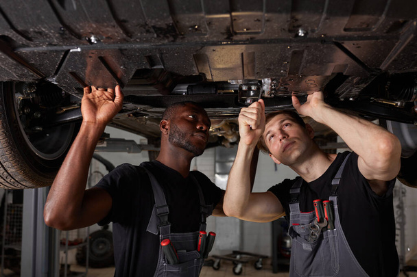 two car mechanics in uniform checking car in automobile service with lifted vehicle - Foto, imagen