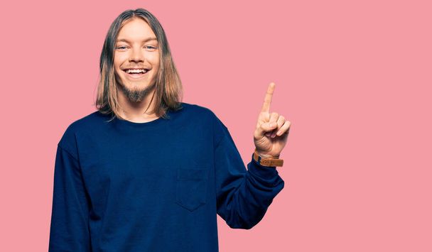 Handsome caucasian man with long hair wearing casual winter sweater pointing finger up with successful idea. exited and happy. number one.  - Фото, зображення