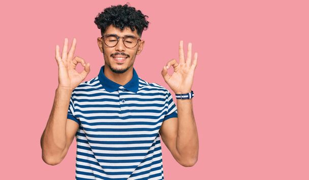 Young arab man wearing casual clothes and glasses relax and smiling with eyes closed doing meditation gesture with fingers. yoga concept.  - Fotografie, Obrázek