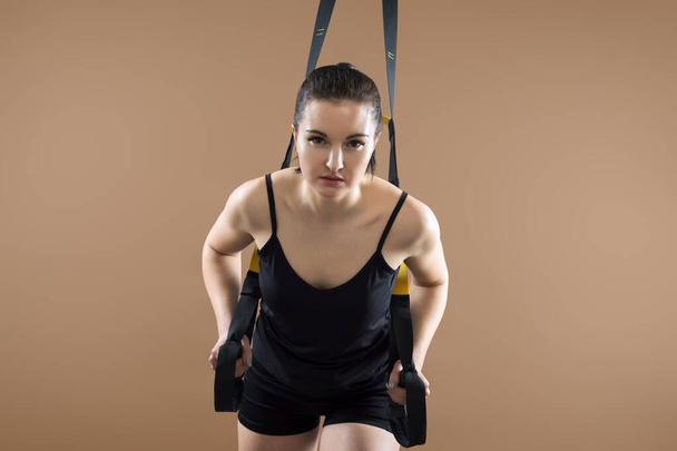 Fitness portrait of young woman with fitness functional loops for training on brown background - Foto, imagen