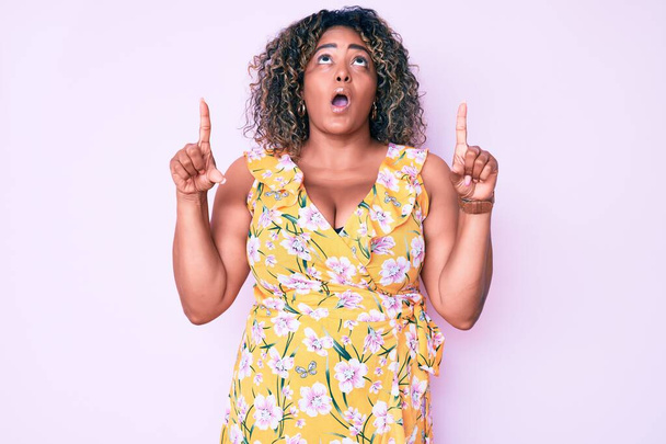 Young african american plus size woman wearing casual clothes amazed and surprised looking up and pointing with fingers and raised arms.  - Photo, Image