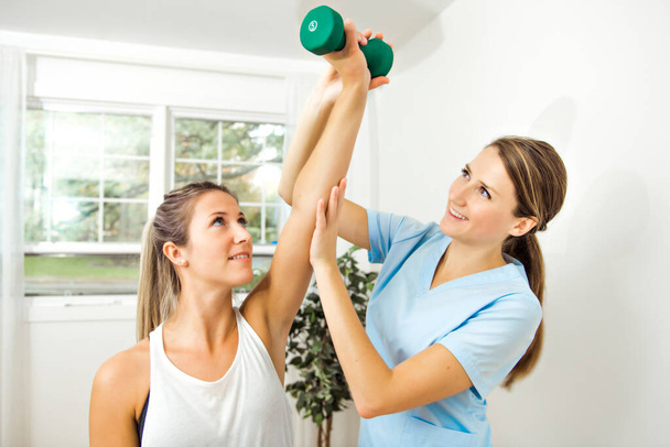 A Modern rehabilitation physiotherapist at work with client. Working on shoulder with dumbell - Foto, Imagen