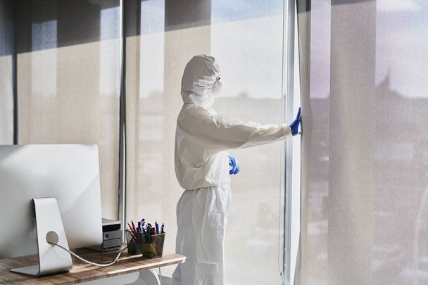 Pessoa em vestuário de trabalho de proteção olhando pela janela                                - Foto, Imagem