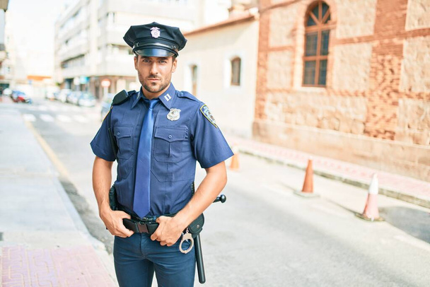 mladý pohledný hispánský policista v policejní uniformě. Stojící s vážným výrazem na ulici. - Fotografie, Obrázek