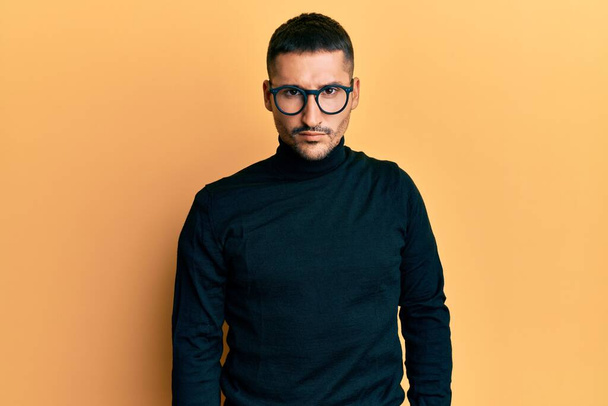 Handsome man with tattoos wearing turtleneck sweater and glasses skeptic and nervous, frowning upset because of problem. negative person.  - Фото, изображение