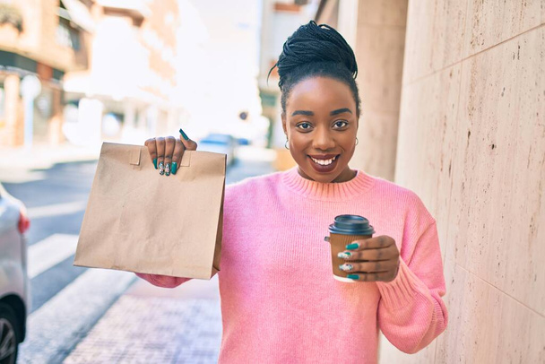 Nuori afrikkalainen amerikkalainen nainen tilalla toimitus paperipussi ja ottaa pois kahvia kaupungin. - Valokuva, kuva