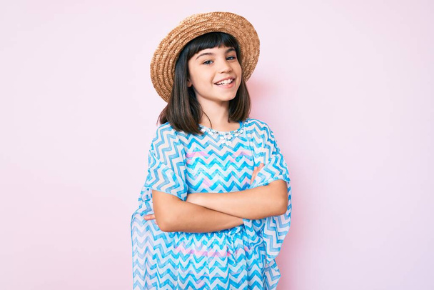 Young little girl with bang wearing summer dress and hat happy face smiling with crossed arms looking at the camera. positive person.  - Foto, immagini