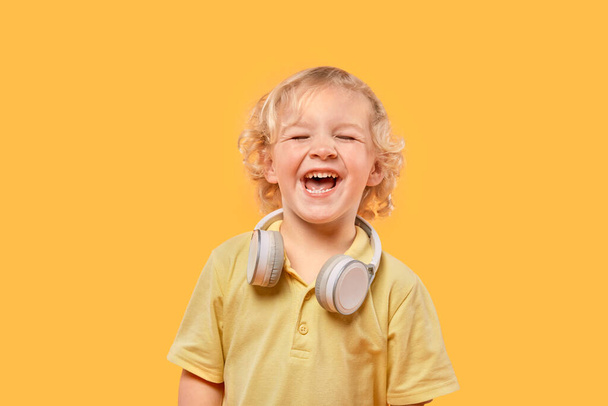 Beautiful happy boy with curly blond hair listening to music. - Фото, зображення