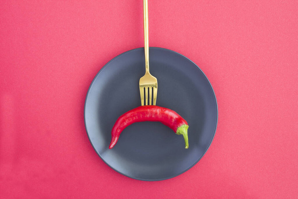 Chili peper gespietst op een gouden vork op de zwarte plaat op de rode achtergrond - Foto, afbeelding