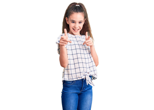 Carino ispanico bambino ragazza indossa abiti casual puntando il dito verso la fotocamera con viso felice e divertente. buona energia e vibrazioni.  - Foto, immagini