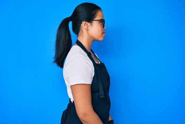 Young beautiful asian girl wearing professional apron looking to side, relax profile pose with natural face with confident smile.  - Φωτογραφία, εικόνα