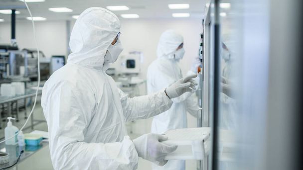 In the Manufacturing Facility Team of Scientist Wearing Sterile Protective Coverall Sets up Programs Modern Industrial 3D Printer, High Precision Manufacture of Semiconductors under Process. - Фото, зображення