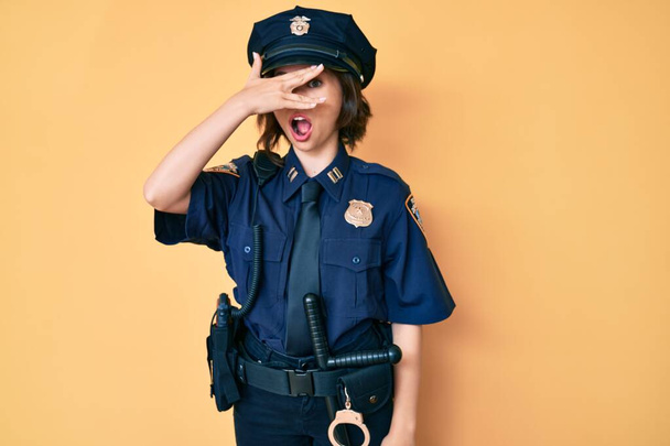 若いです美しいです女性を身に着けています警察制服の目でショックカバー顔と目で手で,恥ずかしい表情で指を通して見て.  - 写真・画像