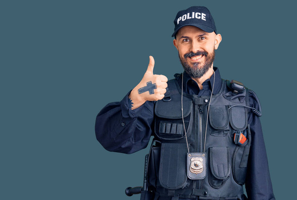 警察の制服を着た若いハンサムな男が手で幸せな親指を振る舞います。成功を示すカメラを見ると.  - 写真・画像