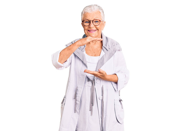 Senior beautiful woman with blue eyes and grey hair wearing casual clothes and glasses gesturing with hands showing big and large size sign, measure symbol. smiling looking at the camera. measuring concept.  - Foto, Bild