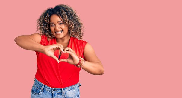 Young african american plus size woman wearing casual style with sleeveless shirt smiling in love doing heart symbol shape with hands. romantic concept.  - Fotoğraf, Görsel