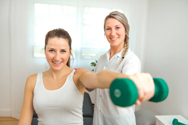 A Modern rehabilitation physiotherapist at work with client. Working on shoulder with dumbell - Fotoğraf, Görsel