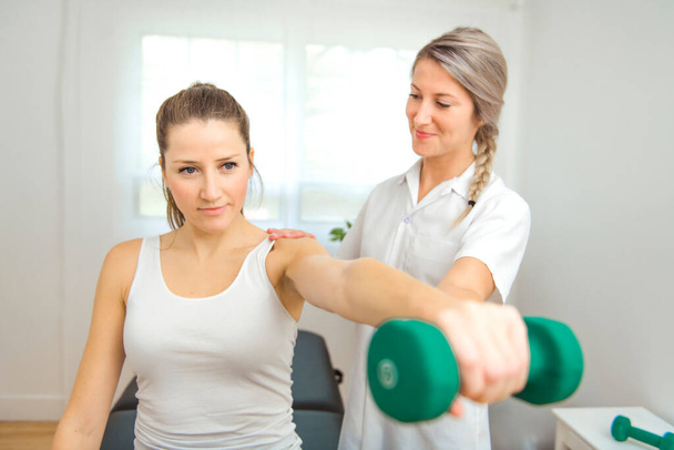 A Modern rehabilitation physiotherapist at work with client. Working on shoulder with dumbell - Foto, afbeelding