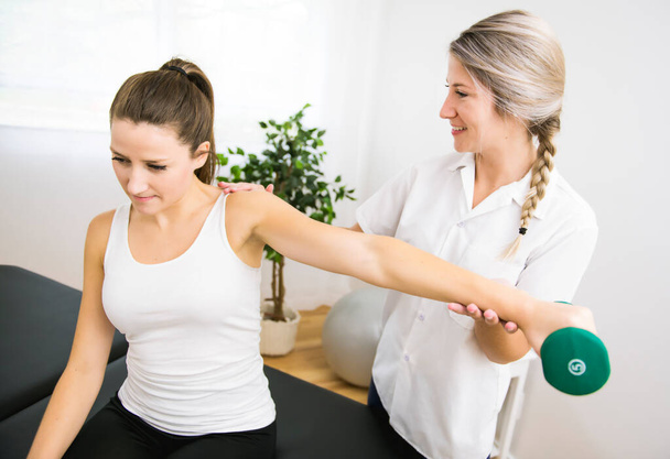 A Modern rehabilitation physiotherapist at work with client. Working on shoulder with dumbell - Fotografie, Obrázek