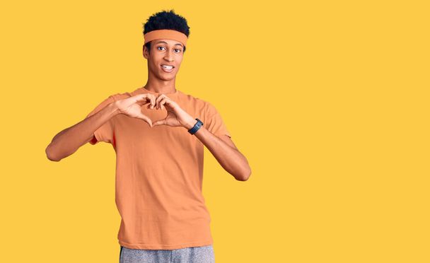 Ein junger afrikanisch-amerikanischer Mann in Sportbekleidung, der verliebt lächelt und das Herzsymbol und die Form mit den Händen zeigt. Romantisches Konzept.  - Foto, Bild
