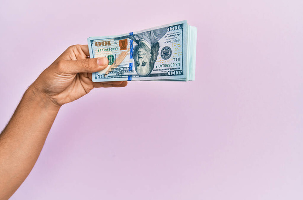Hispanic hand holding usa dollars banknotes over isolated pink background. - Φωτογραφία, εικόνα