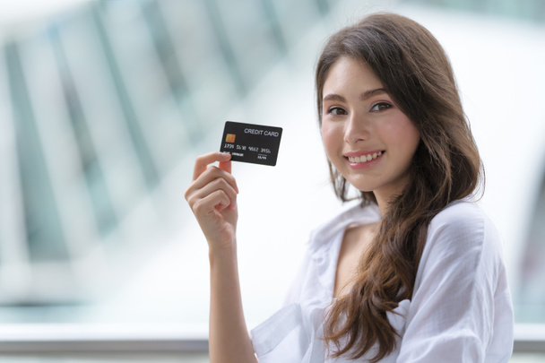 Concepto Viernes Negro, Mujer sosteniendo tarjeta de crédito y sonriendo cerca de la tienda durante el proceso de compra - Foto, imagen