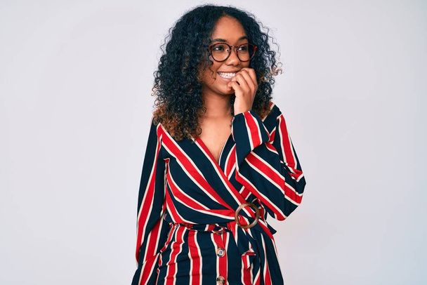Jonge Afro-Amerikaanse vrouw draagt casual kleren en glazen die er gestrest en nerveus uitzien met handen op de mond bijtende nagels. angstprobleem.  - Foto, afbeelding