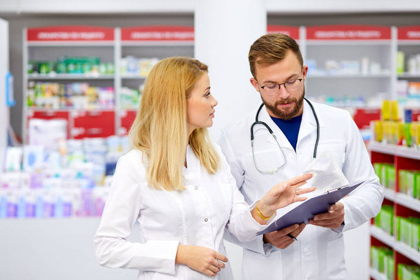 confident male and female druggists talk in pharmacy - Foto, imagen