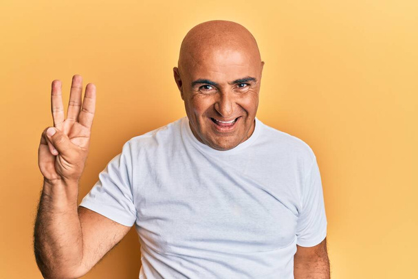 Kypsä Lähi-idän mies päällään rento valkoinen t paita osoittaa ja osoittaa sormilla numero kolme hymyillen itsevarma ja onnellinen.  - Valokuva, kuva