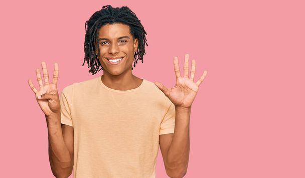 Fiatal afro-amerikai férfi alkalmi ruhát visel, kilences számú ujjal mutogat, miközben magabiztosan és boldogan mosolyog..  - Fotó, kép