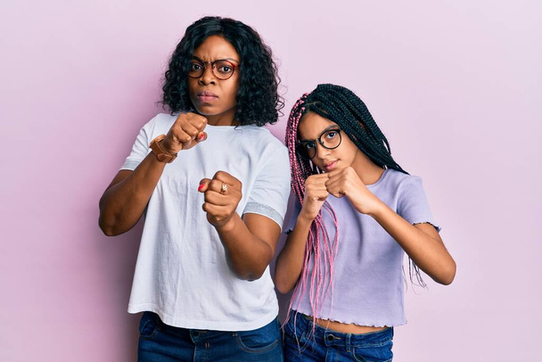 Schöne afrikanisch-amerikanische Mutter und Tochter tragen lässige Kleidung und Brille Faustschlag zum Kampf, aggressive und wütende Angriffe, Bedrohung und Gewalt  - Foto, Bild