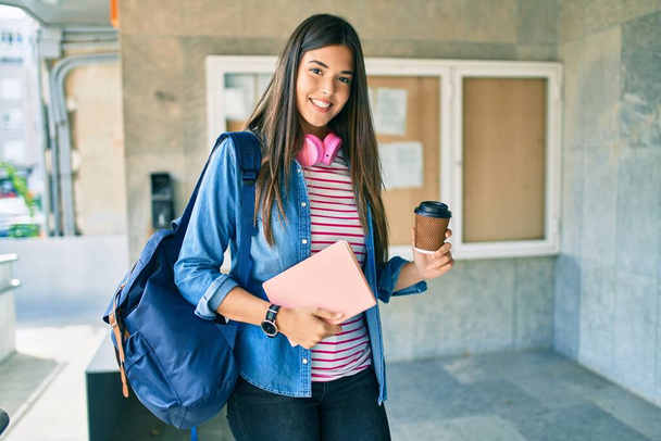 Молода студентка-іспанка посміхається щасливо тримає книгу і п'є каву в університеті
. - Фото, зображення