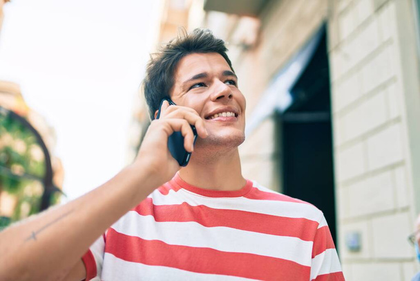 Joven hombre caucásico sonriendo feliz hablando en el teléfono inteligente en la ciudad. - Foto, Imagen