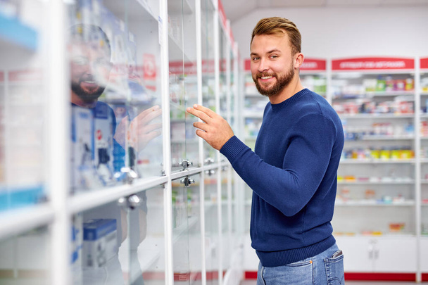 smiling client man standing near medicine shelf - Foto, Bild