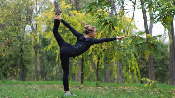 Młoda kobieta ćwiczy jogę w parku miejskim na trawie - Materiał filmowy, wideo