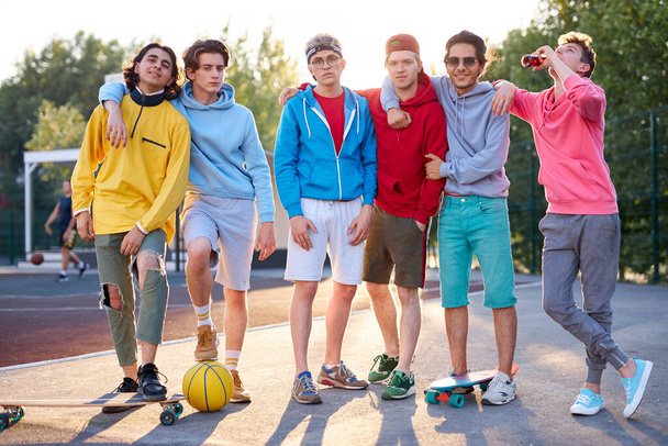 portrait of friendly team of sportive teenagers holding basketball ball and skateboard - Foto, afbeelding