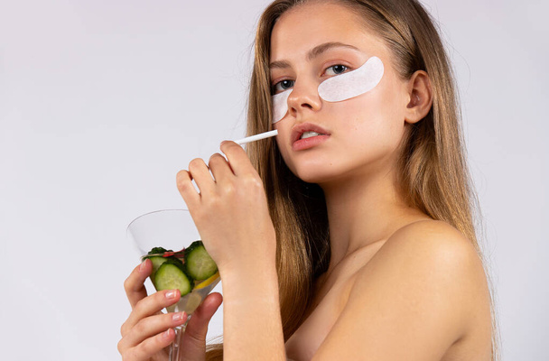 Side portrait of a beautiful young girl with long hair, eye drops and a cocktail in her hands. Skin care and healthy food concept. Photo on white background. High quality photo - Valokuva, kuva
