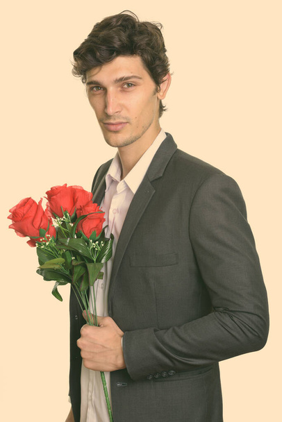 Studio zdjęcie młodego przystojnego biznesmena trzymającego czerwone róże - Zdjęcie, obraz